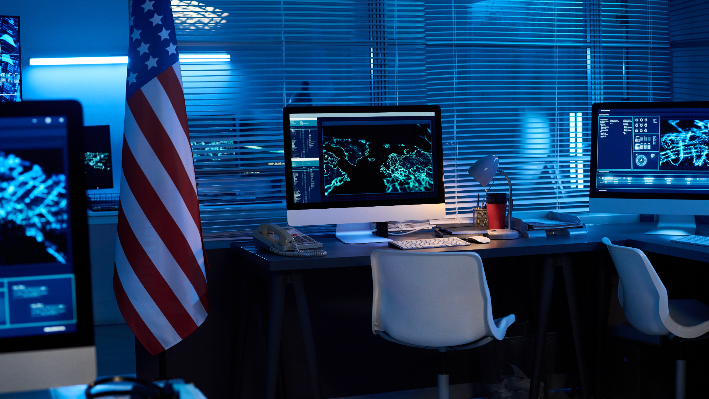 An unattended analyst workstation at night, screens live and a US flag beside the desk